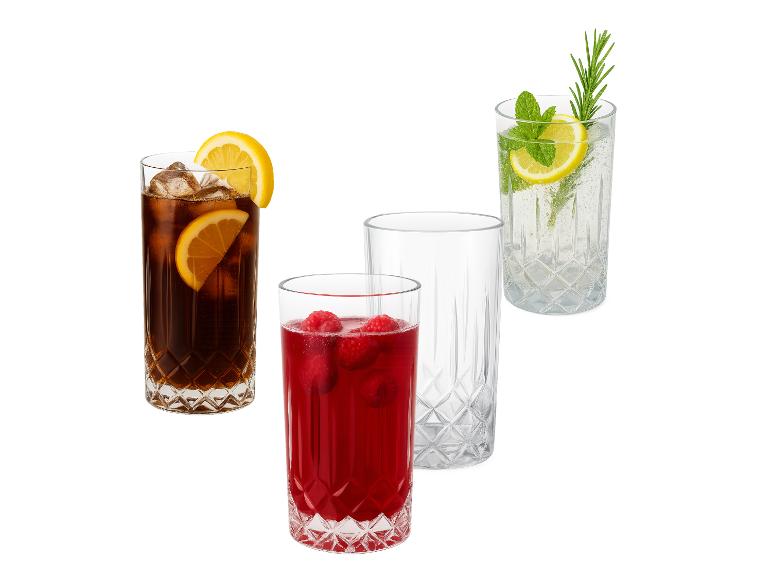Quatre verres en verre, un avec du cola, un avec une boisson à la framboise, un vide et un avec de l'eau pétillante.