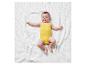 Bébé sur une couverture blanche portant un body jaune.