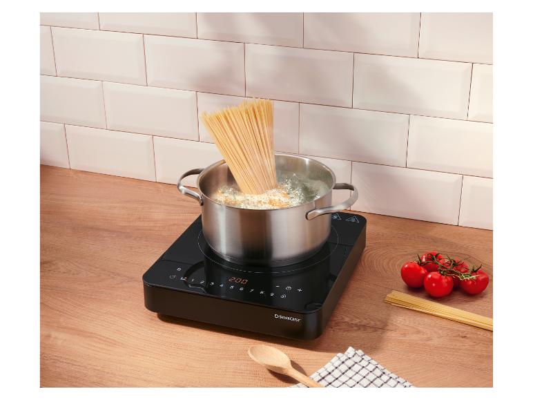 Cuisson de spaghettis dans une casserole sur une plaque à induction, tomates et spaghettis crus sur le comptoir.