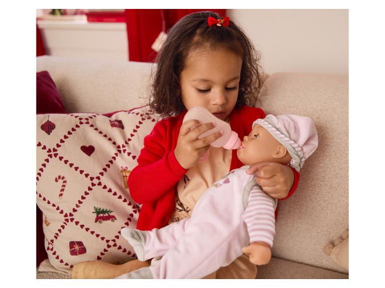 Une jeune fille nourrit une poupée avec un biberon sur un canapé.