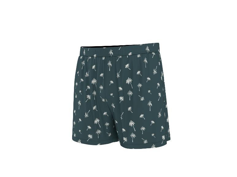 Short de bain vert foncé avec motif de palmiers blancs.