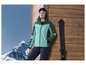 Une femme en veste de ski verte avec des skis et des gants.