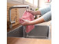 Femme rinçant un chiffon en microfibre rose sous un robinet de cuisine en acier inoxydable.