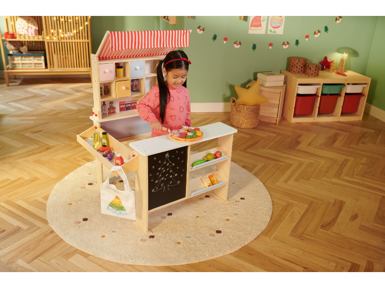 Fille jouant avec un magasin de jouets en bois, décoré dans un style de Noël.