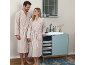 Couple en peignoirs beiges se souriant dans une salle de bain moderne.