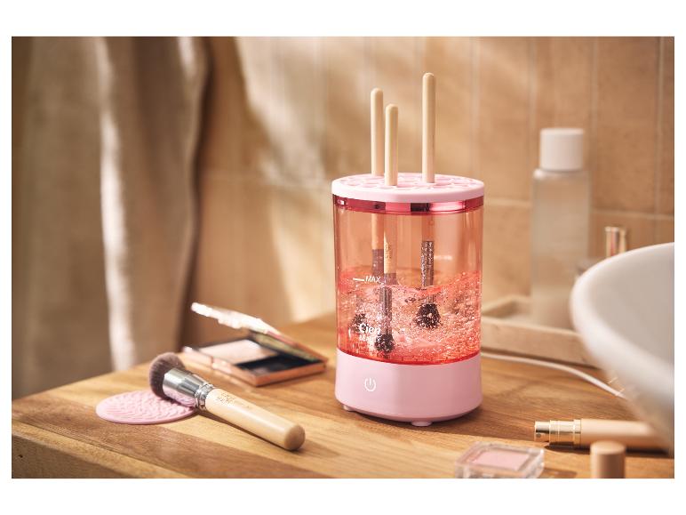 Nettoyeur de pinceaux de maquillage rose avec pinceaux à l'intérieur, sur un comptoir en bois.