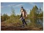 Femme en imperméable beige et bottes en caoutchouc bleues marchant près d'un lac.