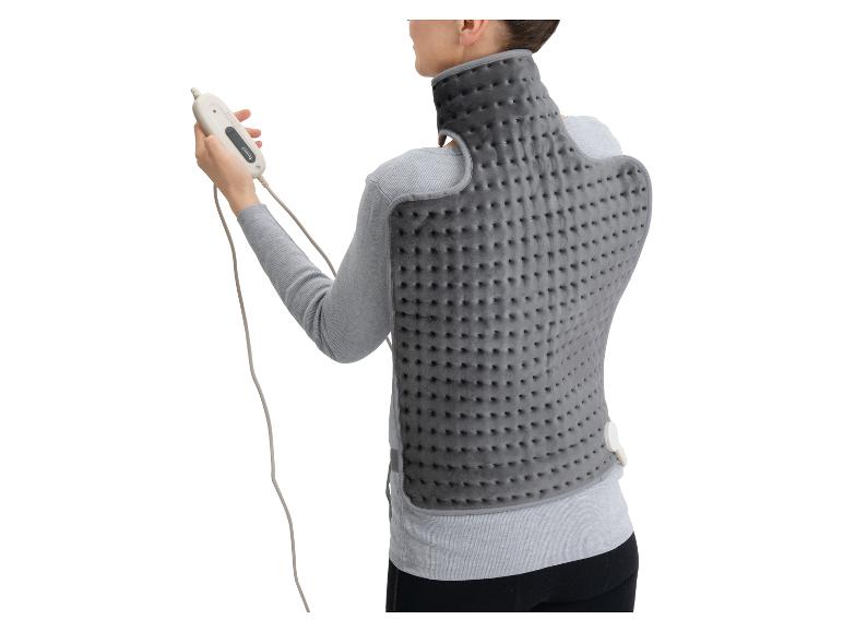 Femme portant un coussin chauffant gris pour le dos et le cou, tenant une télécommande.