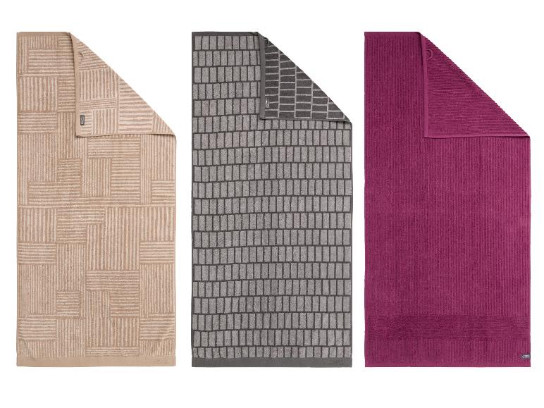 Trois serviettes de bain : beige à motifs géométriques, grise à motifs de briques et violette unie.