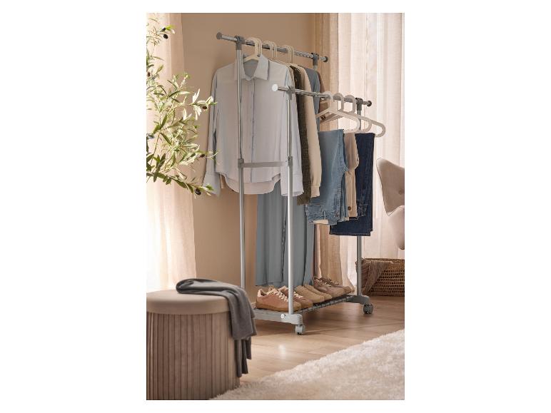 Un portant mobile avec des vêtements, des chaussures et un pouf dans une pièce.