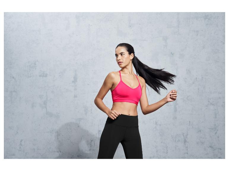 Une femme portant un soutien-gorge de sport rose et un legging noir pose devant un fond gris.