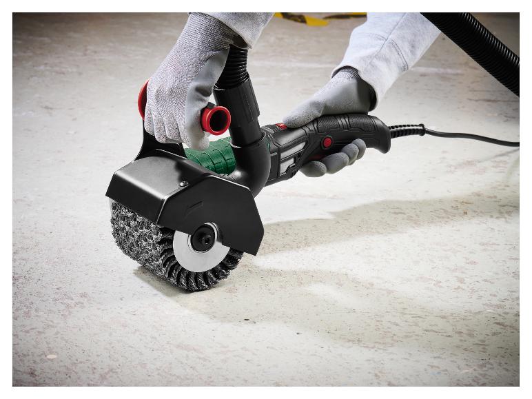 Outil de brossage électrique avec brosse métallique, tenu par des mains gantées sur un sol en béton.