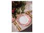 Une table de Noël dressée avec de la vaisselle à fleurs rouges et des couverts dorés.