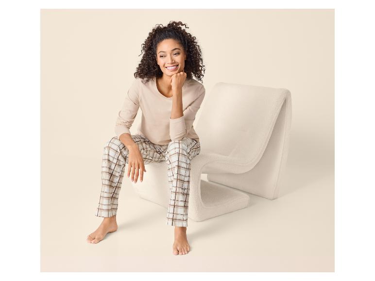 Femme en haut à manches longues beige et pantalon de pyjama à carreaux assise sur une chaise moderne.