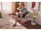 Homme en short et sandales, assis dans un fauteuil dans un salon moderne.