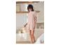 Femme souriante en pyjama rose clair, t-shirt et short, dans une chambre lumineuse.