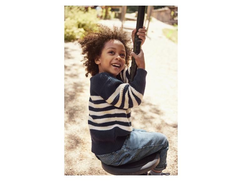 Un garçon heureux en pull rayé et jean sur une balançoire.