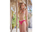 Une femme en bikini rose à imprimé tropical sur la plage.