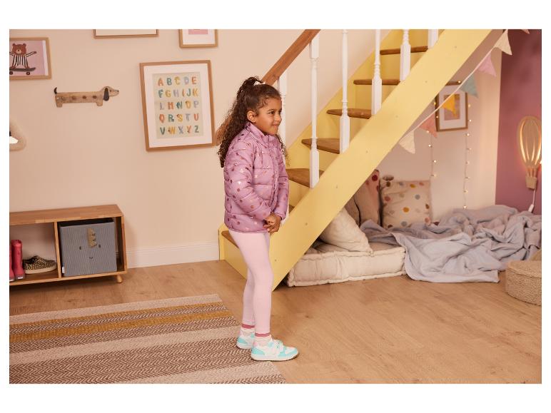 Jeune fille en doudoune rose et leggings rose clair dans une chambre ludique.