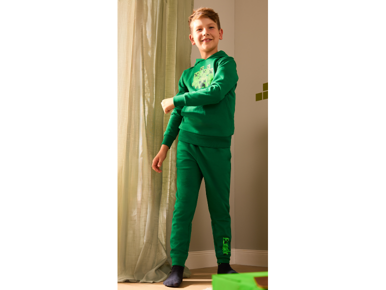 Garçon souriant en sweat à capuche vert et pantalon de jogging avec imprimé monstre.