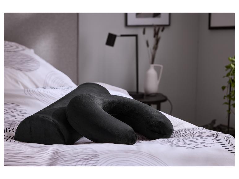 Oreiller de voyage noir et traversin sur un lit avec des draps à motifs.