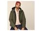 Homme en doudoune verte, pull beige à demi-zip, jean foncé et bonnet rouge.