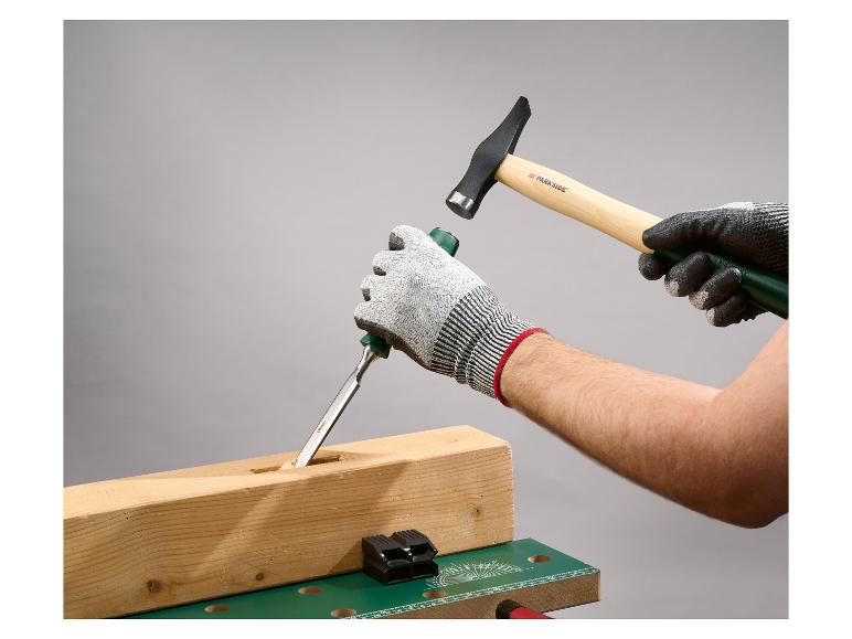 Des mains gantées utilisent un ciseau et un marteau pour travailler une poutre en bois.