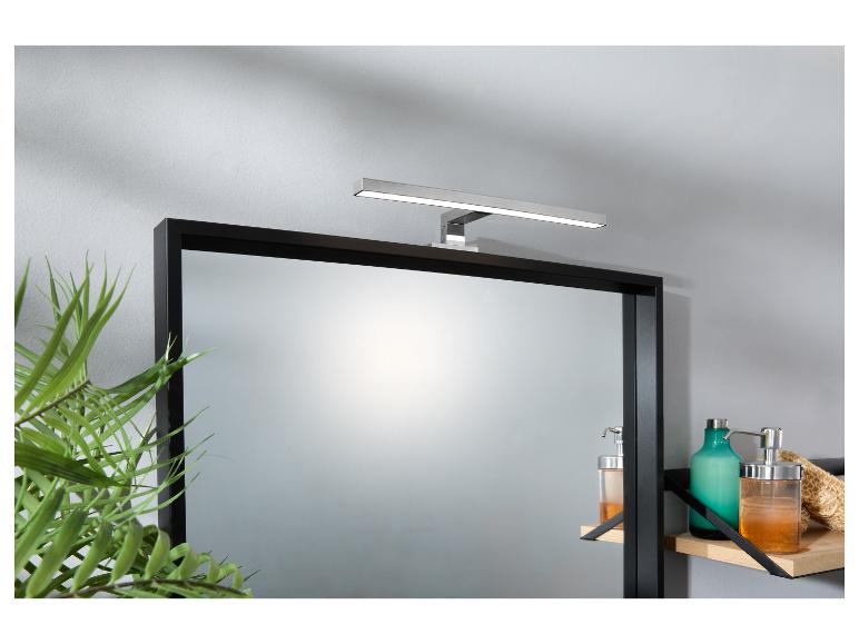 Un miroir de salle de bain avec une lampe LED horizontale au-dessus et des produits de bain sur une étagère.