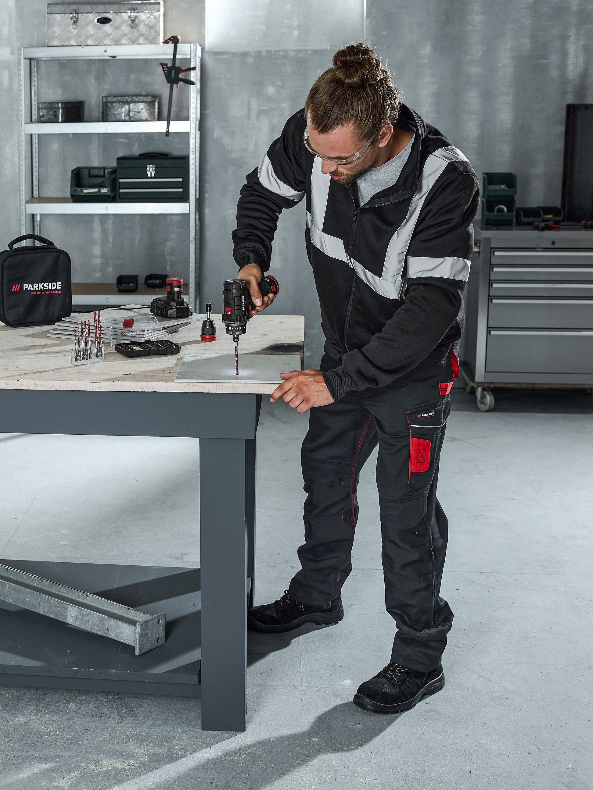 Homme perçant une surface avec une perceuse sans fil, entouré de divers forets et outils.