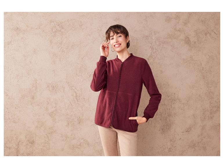 Une femme porte une veste en polaire bordeaux à fermeture éclair.