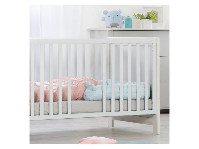 Lit de bébé blanc avec literie rose et bleue, avec des jouets en peluche.