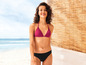 Une femme en bikini rose sur une plage avec un fond en osier.