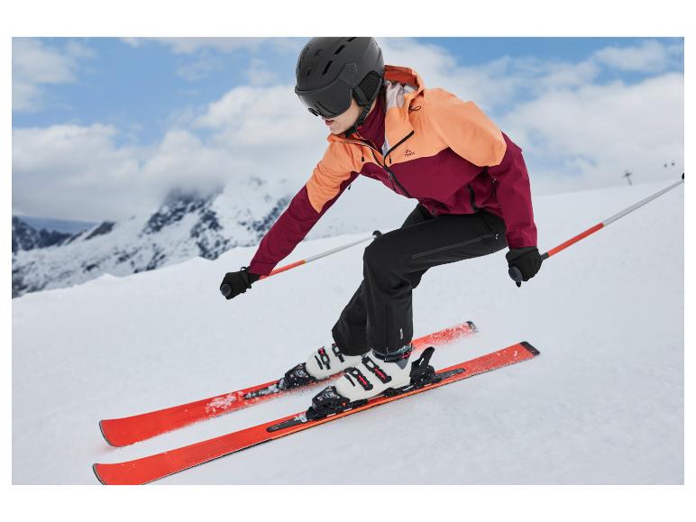 Une femme skie sur une pente de montagne, vêtue d'une veste de ski Crivit et d'un pantalon noir.