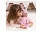 Fille jouant avec une poupée bébé en tenue rose sur un tapis blanc.