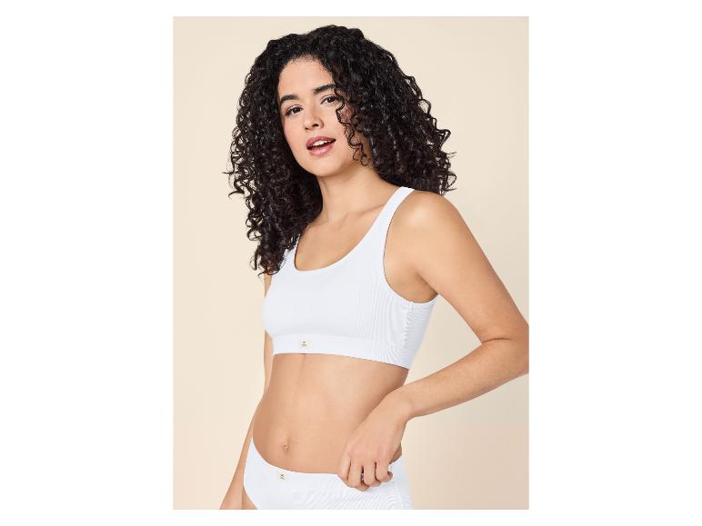 Femme aux cheveux bouclés portant une brassière côtelée blanche et une culotte assortie.