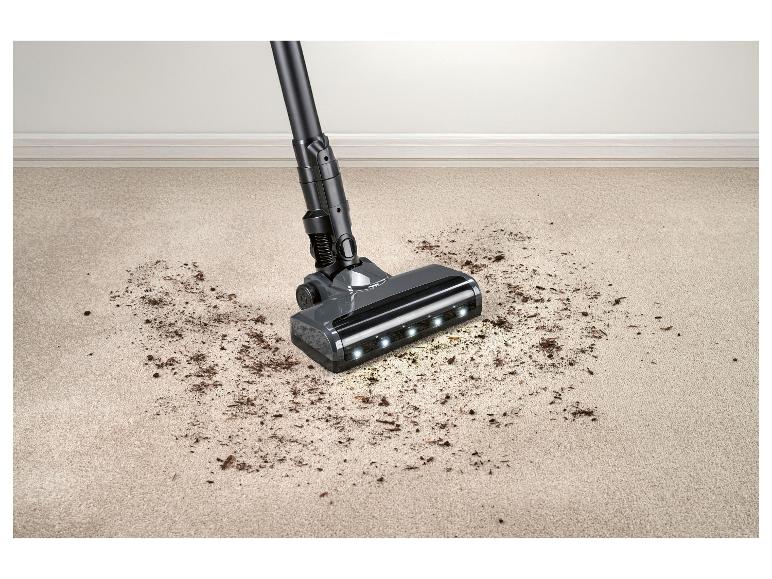 Aspirateur balai nettoyant un tapis, débris au sol.