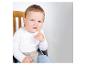 Un bébé en chemise blanche et pantalon bleu assis dans une chaise haute, le doigt dans la bouche.