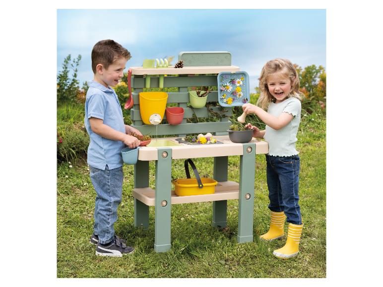 Deux enfants jouent avec une table de jardin Smoby à l'extérieur.