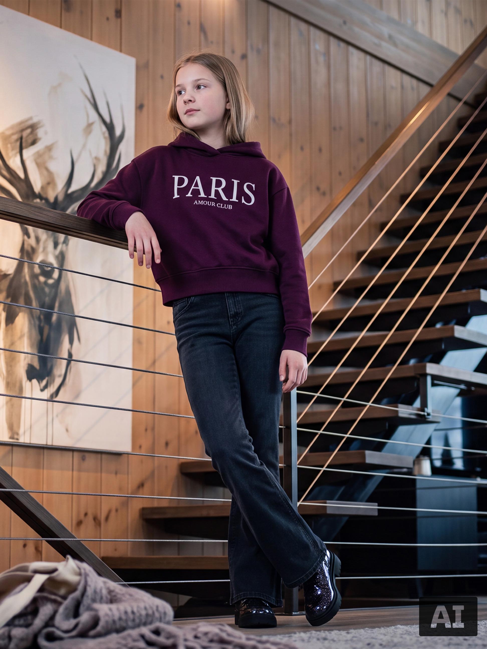 Fille en sweat à capuche bordeaux avec inscription Paris et jean foncé sur un escalier.