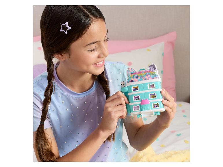 Une fille souriante tient une maison de poupée sur le thème des chats avec de petites figurines.
