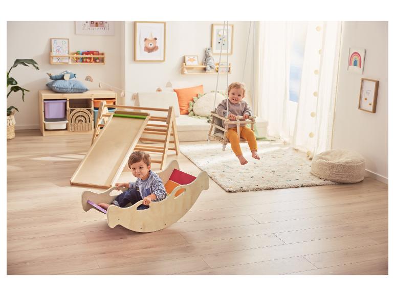 Enfants jouant avec un toboggan en bois, une balançoire et un cheval à bascule dans une salle de jeux.