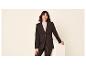 Femme en blazer noir et pantalon en cuir souriant à la caméra.