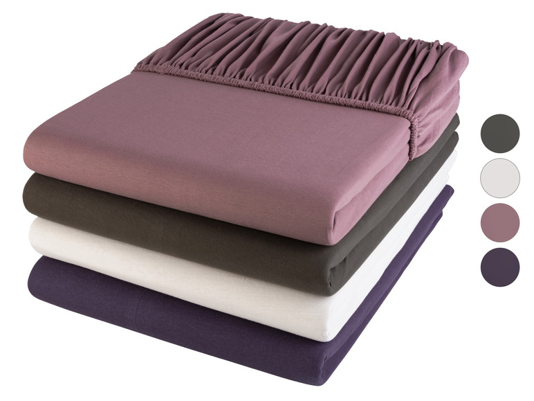 Une pile de quatre draps de lit dans différentes couleurs: rose, gris foncé, blanc et violet.
