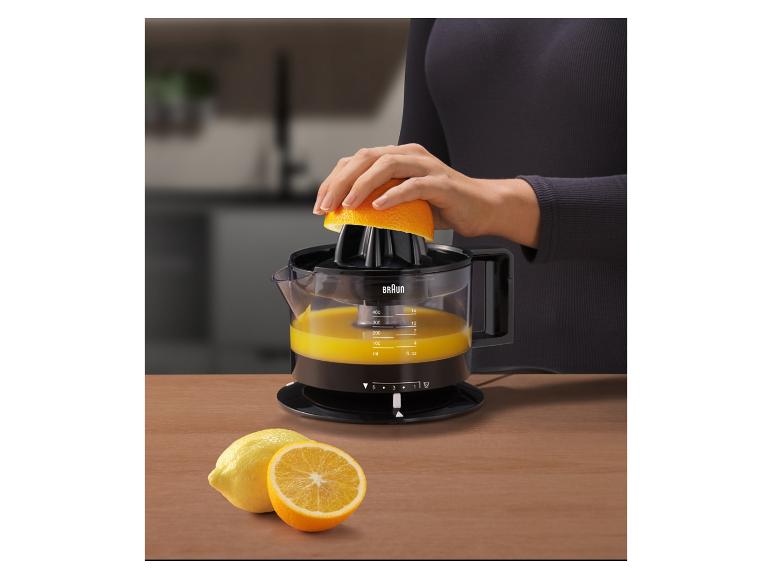 Femme pressant une orange avec un presse-agrumes, avec des citrons et des oranges sur une table en bois.