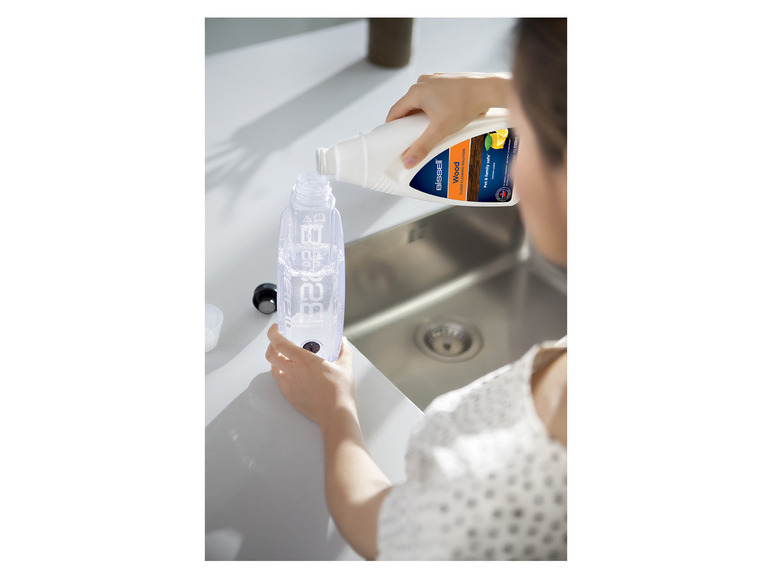 Une femme verse du nettoyant pour sols Bissell Wood dans une bouteille.