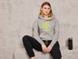 Une femme porte un sweat à capuche gris avec un imprimé léopard de la marque 'JETTÉ SPORT' et un pantalon de jogging noir.