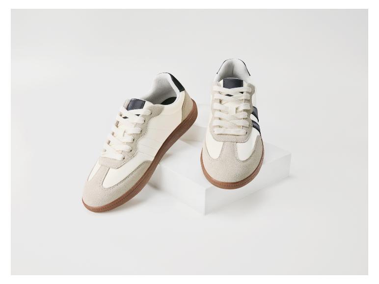 Une paire de baskets crème avec des semelles marron et des détails bleu foncé, présentées sur des boîtes blanches.