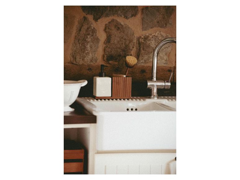Un distributeur de savon en céramique blanche et un porte-brosses en bois se trouvent sur un évier de cuisine.