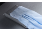 Manchette de chemise bleu clair avec boutons et plis, posée sur un tissu gris.