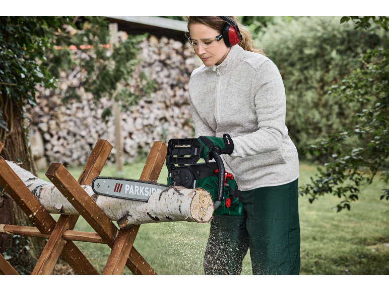 Femme utilisant une tronçonneuse Parkside pour couper des bûches sur un tréteau en bois.